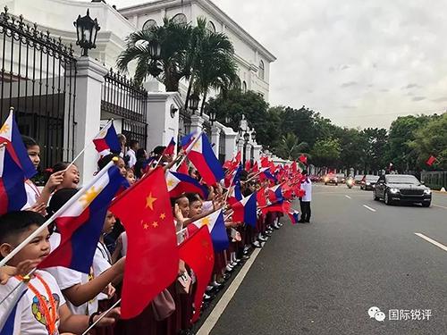 20日,来自马尼拉当地三所小学的千名小学生站在总统府道路两侧挥舞两国国旗,欢迎习主席车队。(图片来源:中央广播电视总台央视新闻 记者邓雪梅拍摄)